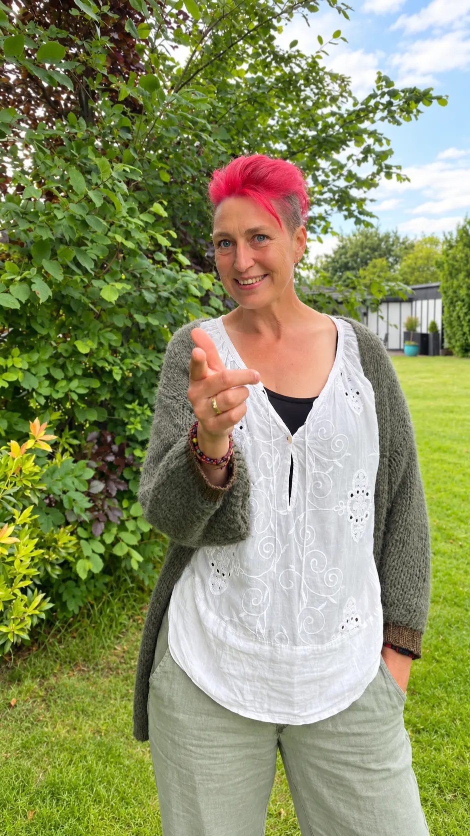 Inge Marie Mørch står i haven, smiler og peger mod dig